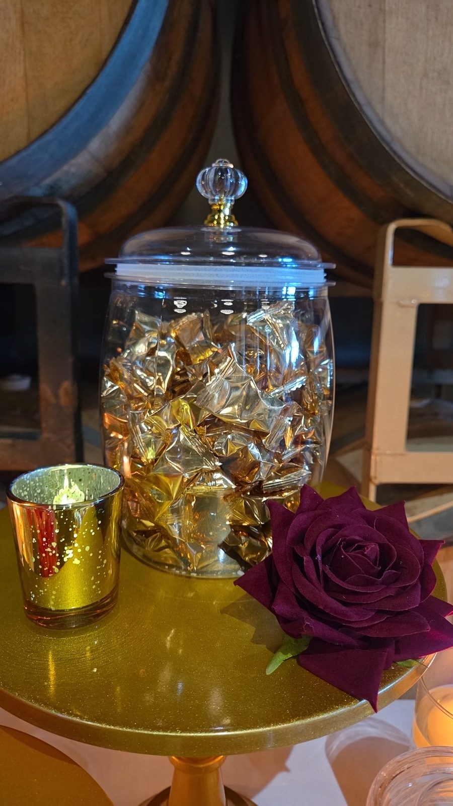 Gold wrapped candies in a glass jar with a burgundy rose